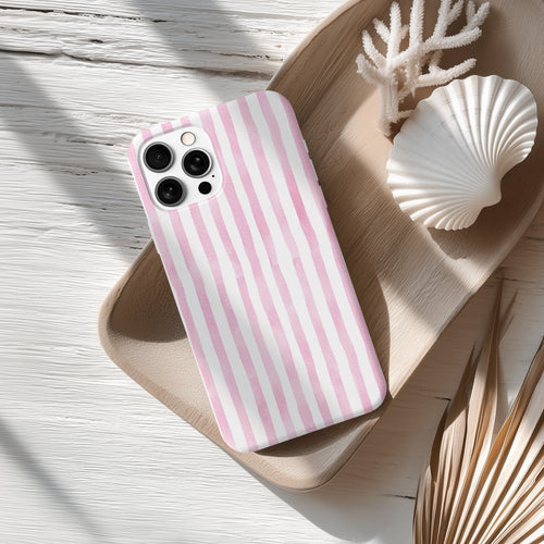 A pink and white striped phone case is placed on a wooden surface, accompanied by a seashell and some dried leaves.