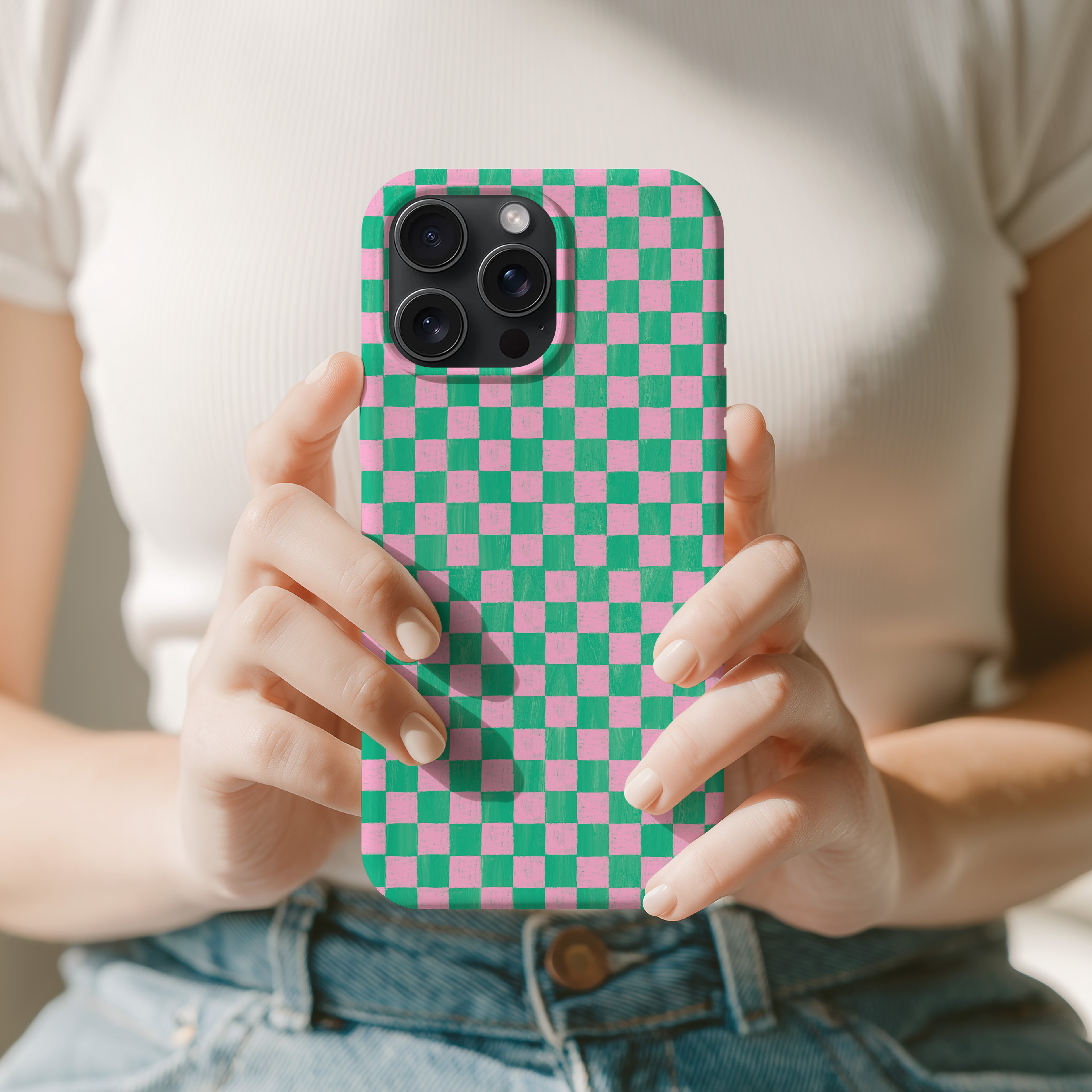A person is holding a phone with a checkered pattern case, wearing a white shirt and blue jeans.