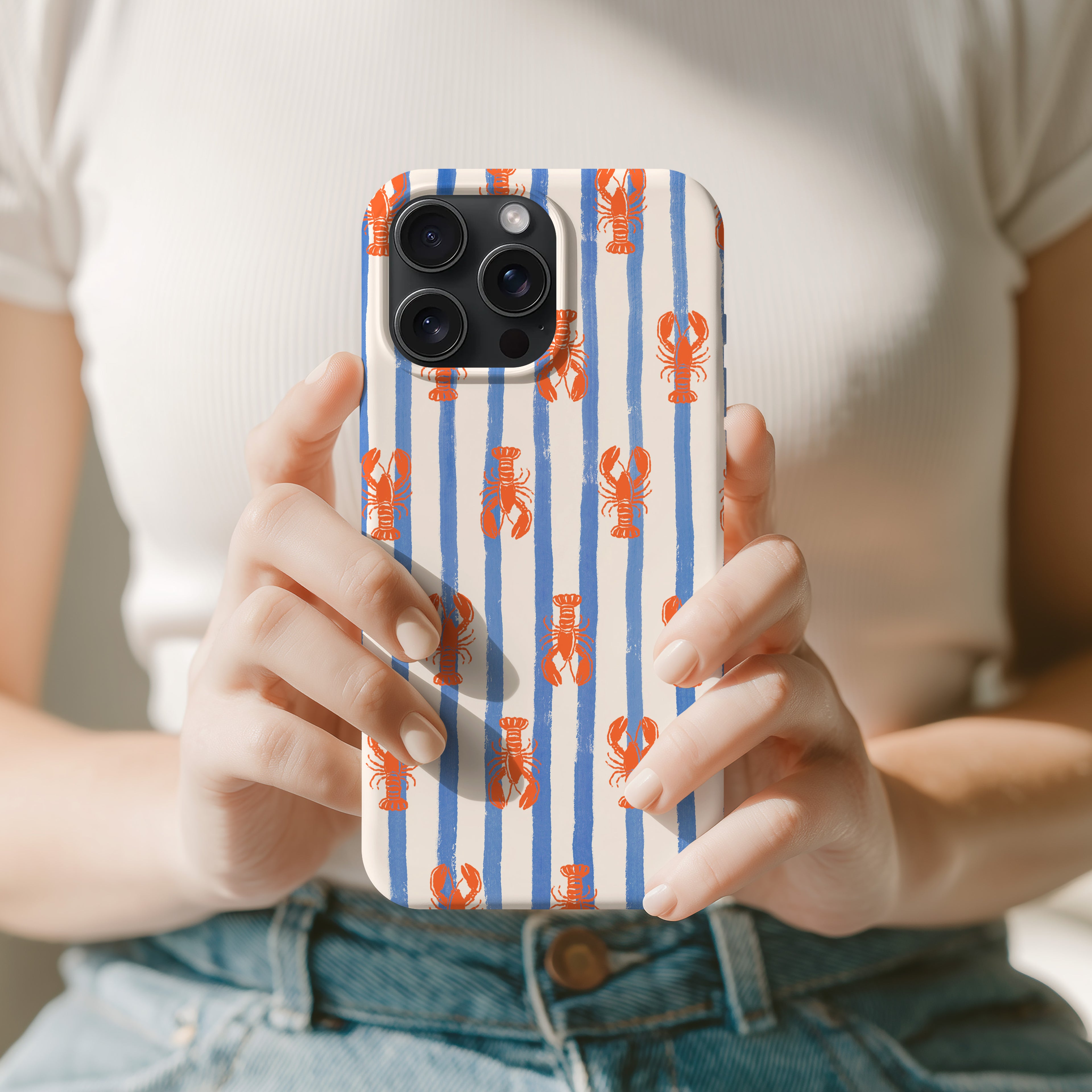A person is holding a phone case with a striped pattern of blue and white stripes and red lobster illustrations.