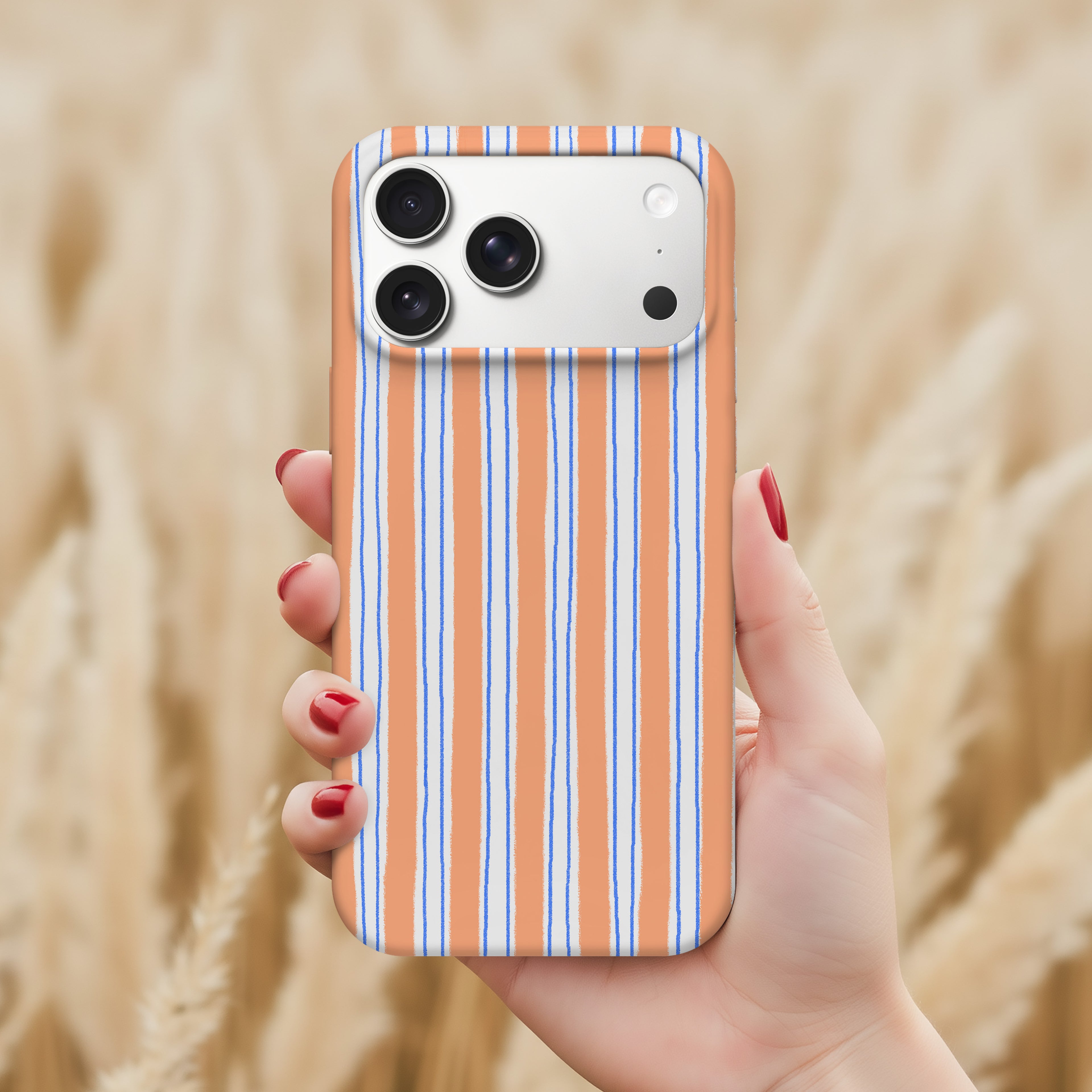 A hand holding a smartphone with a striped pattern on the case, against a blurred background of a field.