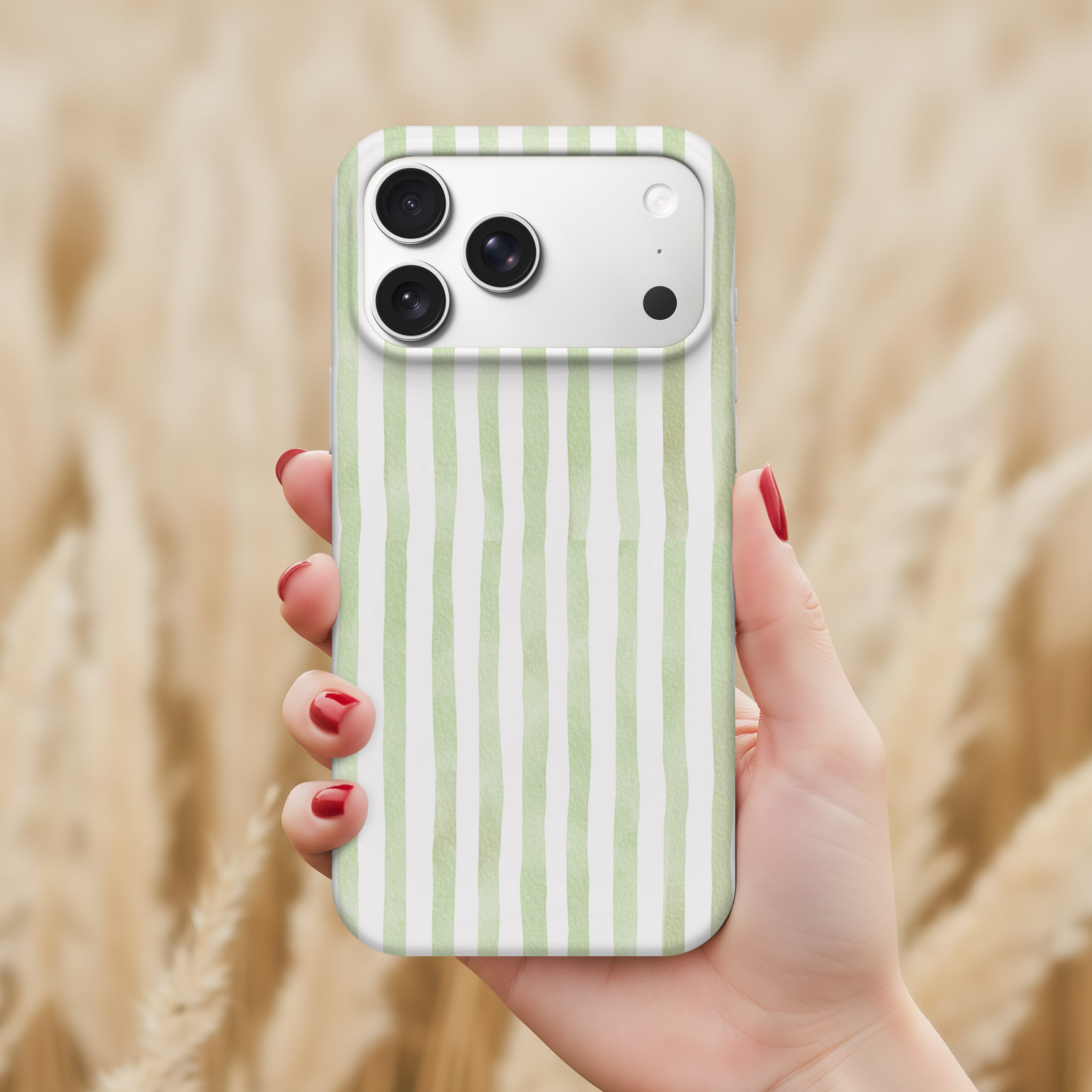 A hand holding a smartphone with a green and white striped patterned case, against a blurred background of a field.