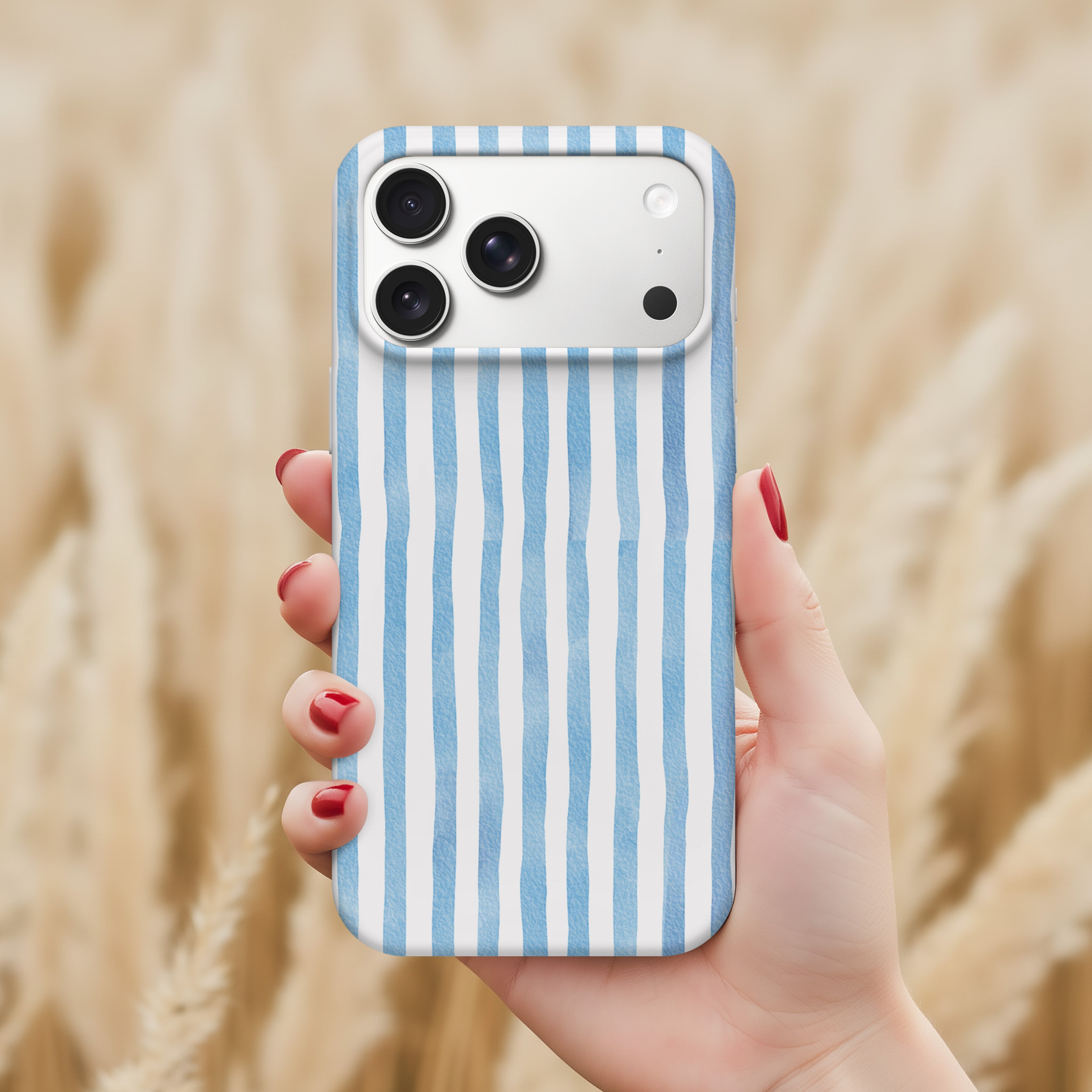 A hand holding a smartphone with a blue and white striped patterned case, against a blurred background of a field.