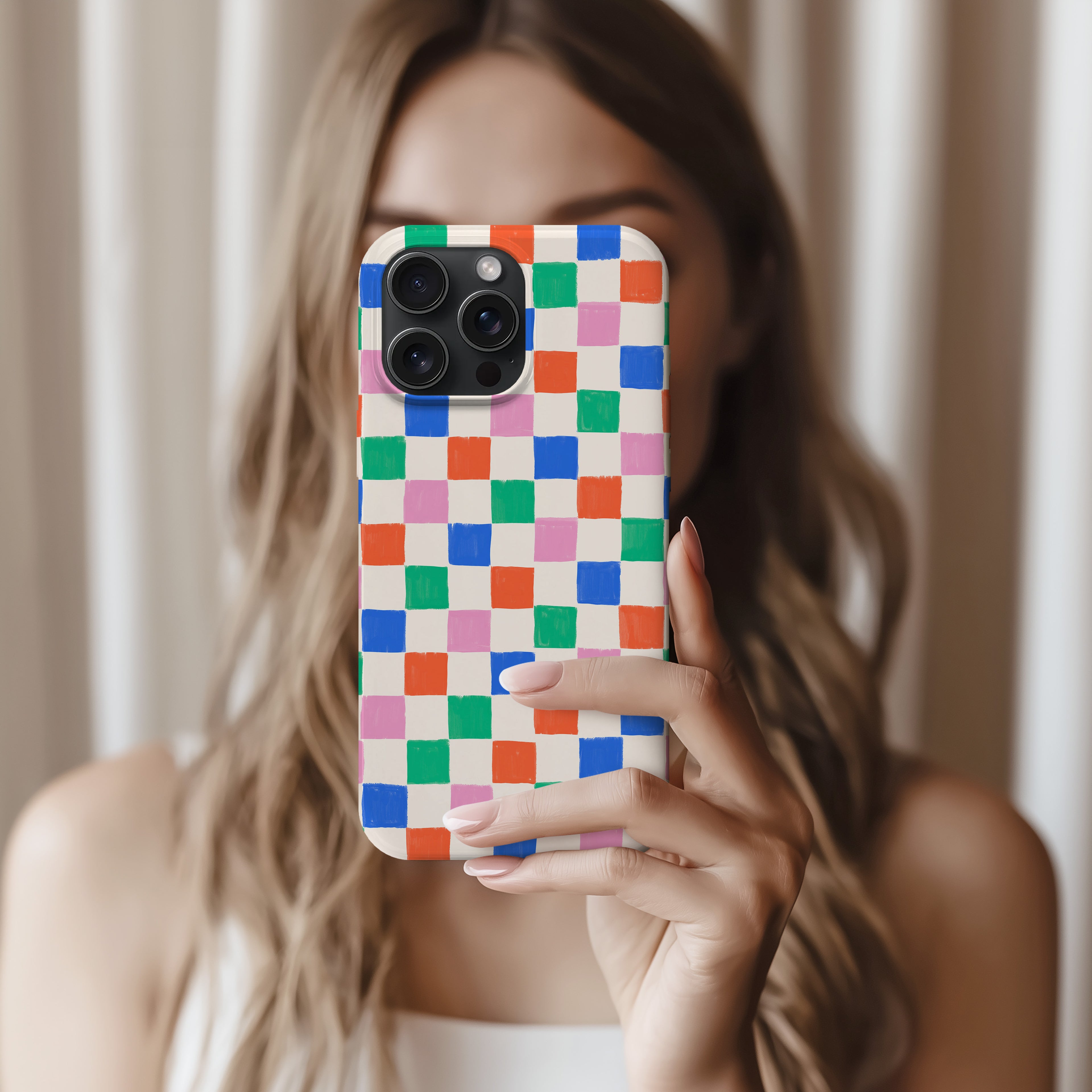 A woman with long, wavy hair is holding a colorful phone case with a checkered pattern.
