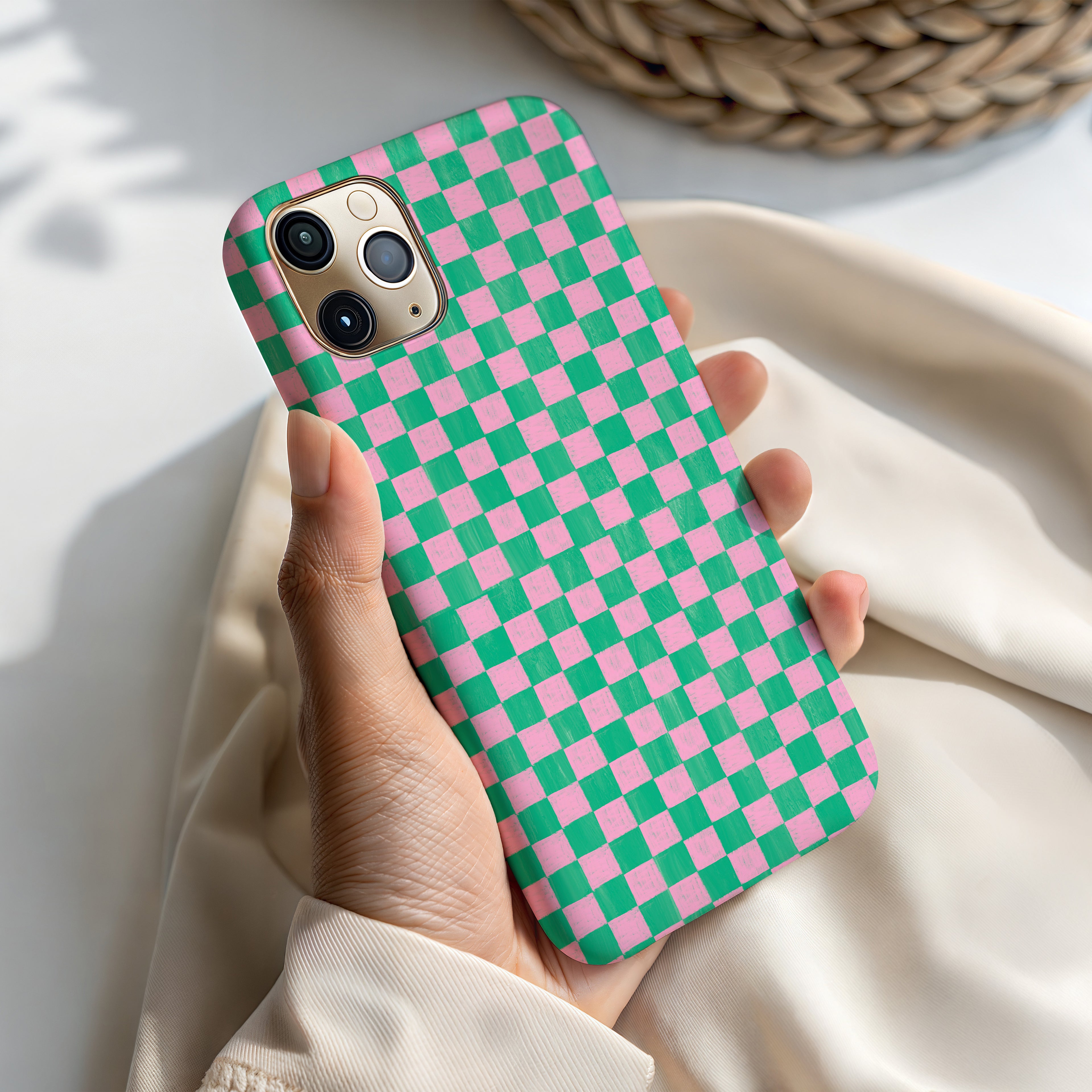 A person's hand holding a phone case with a checkered pattern in pink and green colors.