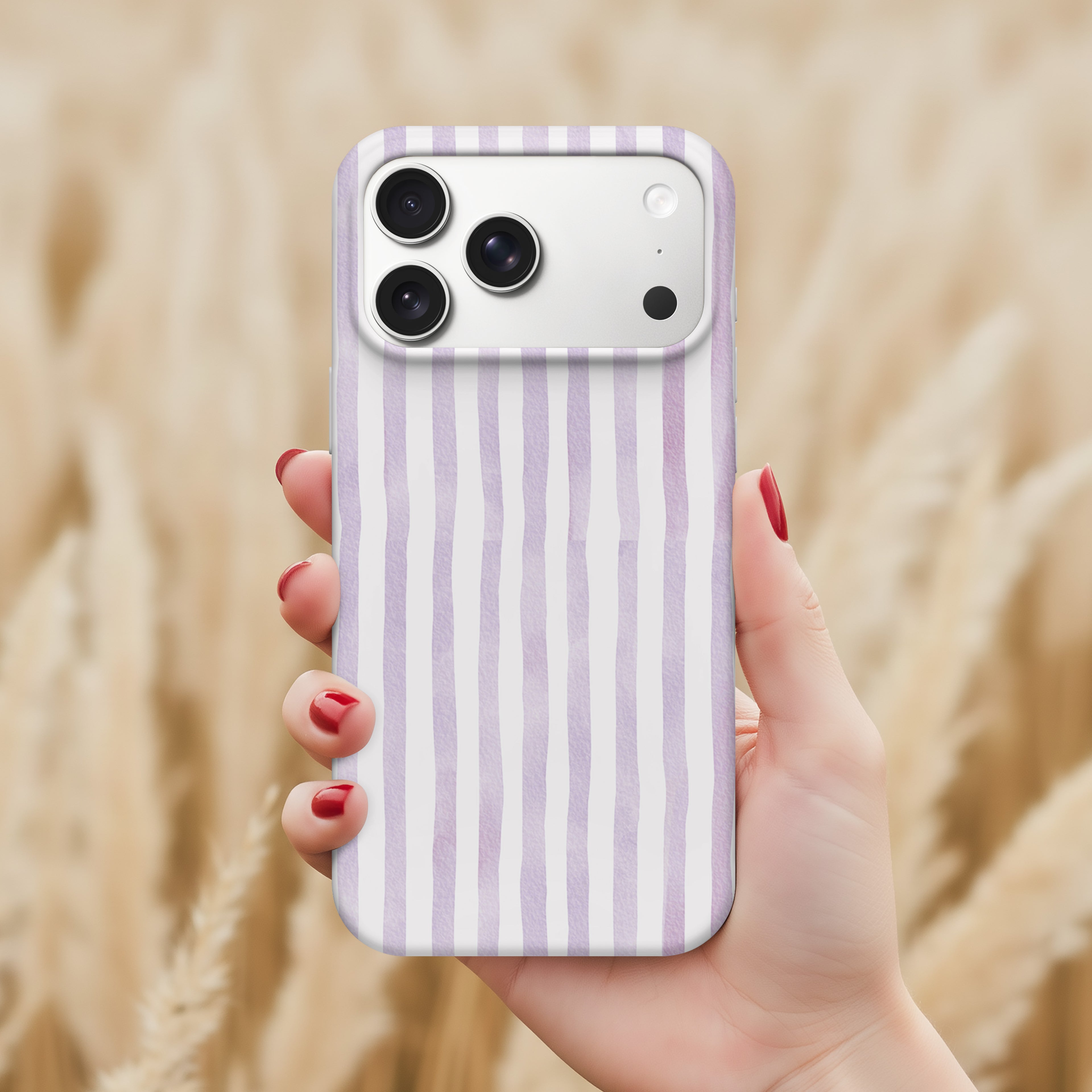 A hand holding a smartphone with a purple and white striped pattern on the back cover, against a blurred background of a field.