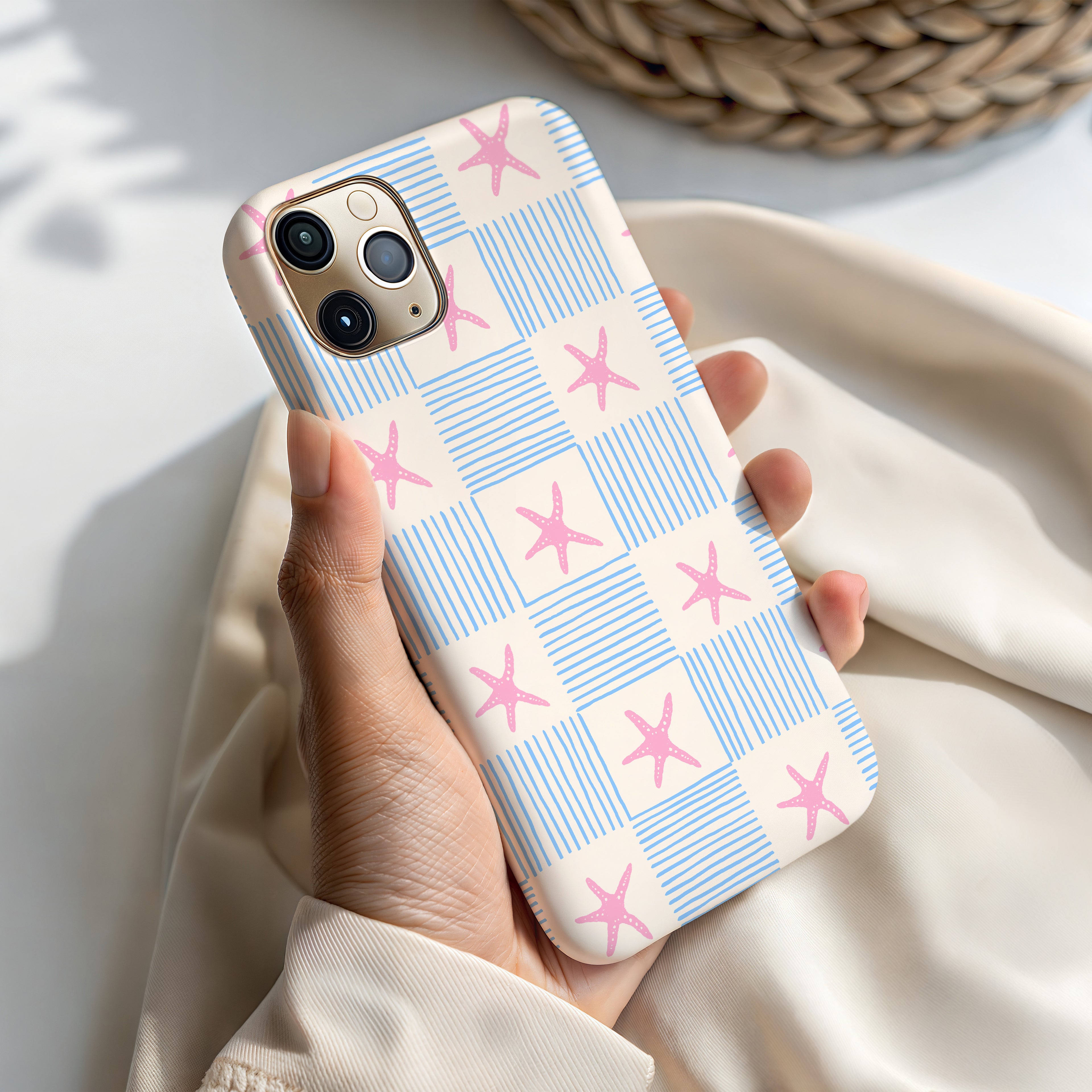 A person's hand holding a phone case with a pattern of blue and white stripes and pink stars.